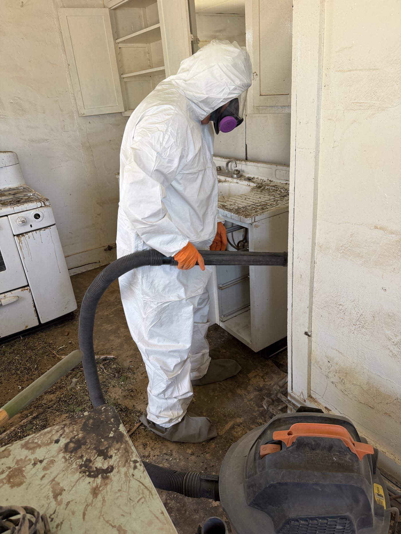 DEKON technician in a protective suit and P100 respirator HEPA vacuuming a water-damaged room
