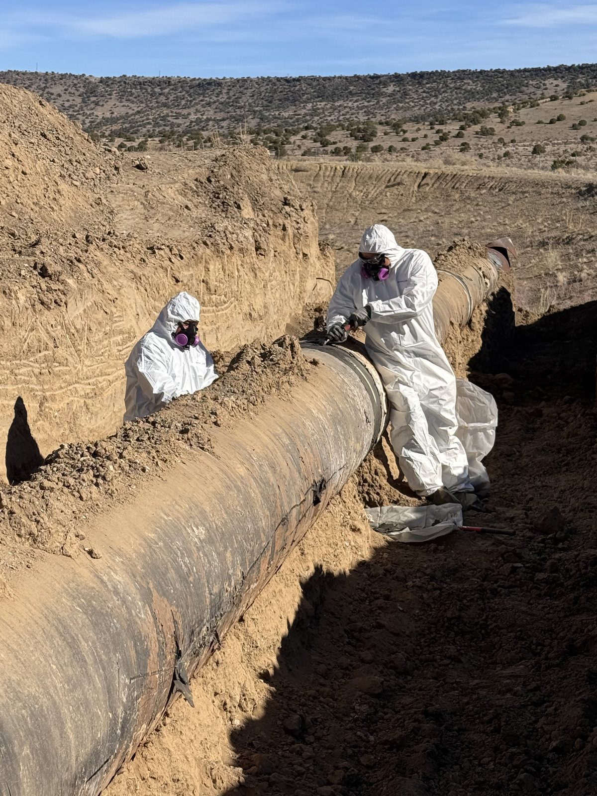 Suited crew handling asbestos cement pipe in the trench